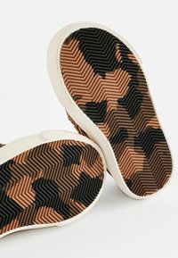 Gummisålar med ett texturerat, zigzag-mönster i svart och nyanser av brunt, med en vit kant runt kanten.
