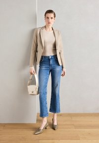 Béžový přizpůsobený blazer, světle ribbované tričko, modré zvonové džíny, zelené nazouvací podpatky a malá béžová kabelka. Čisté linie, neformální chic vzhled.