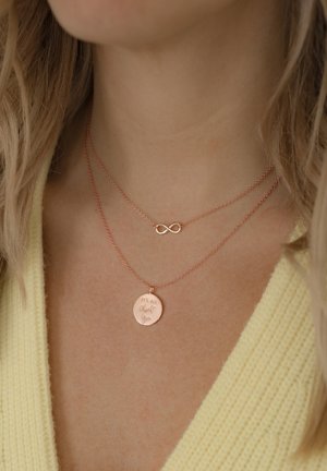 Doppelschichtige Halskette aus Roségold mit einem runden Anhänger, der mit Text und einem Unendlichkeitssymbol graviert ist, und einer glatten Oberfläche.