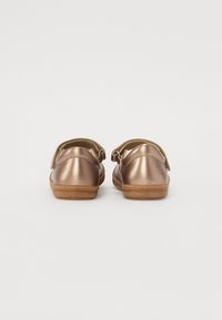 Bronse metalliske sko med glatt overflate, avrundede bakpartier og justerbare stropper. Teksturert såle for bedre grep. Enkelt design, ingen ekstra detaljer.