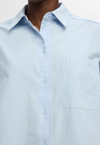 Camicia azzurro chiaro con bottoni realizzata in tessuto liscio, caratterizzata da un colletto classico, bottoni frontali e una tasca sul petto.