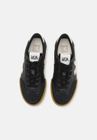 Sneaker nere con tomaia in suede e pelle, caratterizzate da dettagli beige, lacci neri, punta rotonda e suola in gomma color caramello.