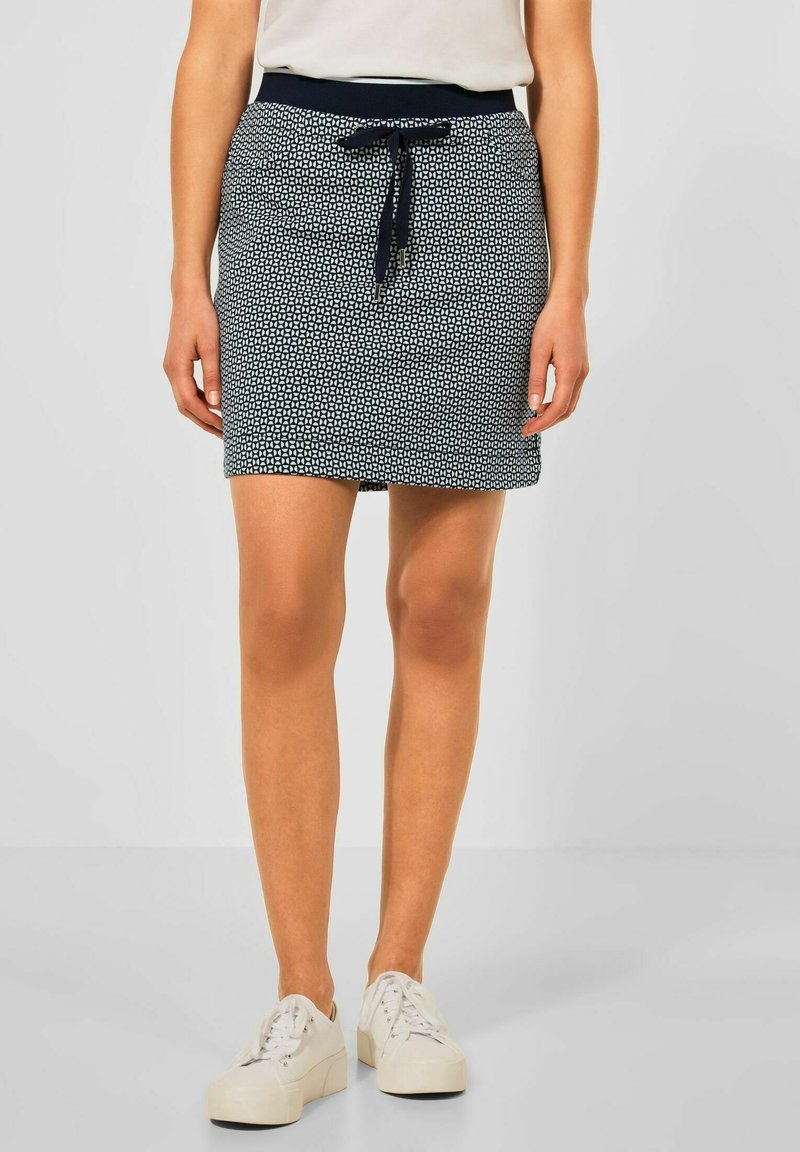 Mörkblå kjol med geometriskt mönster, elastisk midja med snöre, längd ovanför knäna, kombinerad med vita sneakers.