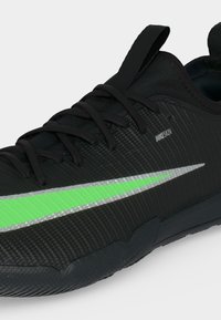 Μαύρο αθλητικό παπούτσι Nike με νεον πράσινο και ασημένιο σήμα, υφή στην επιφάνεια, μαύρα κορδόνια και ταινία τράβηγμα στη γλώσσα.