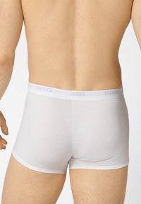 Boxer aderenti bianchi realizzati in un tessuto morbido con una texture liscia. Presentano una cintura elastica bianca con il logo "SLOGGI". Design semplice.