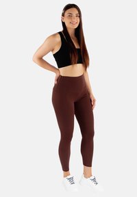 Brązowe legginsy z wysokim stanem z bocznymi kieszeniami, wykonane z gładkiego, elastycznego materiału. W połączeniu z czarnym topem crop i białymi trampkami.