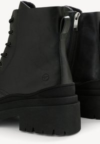 Bottines noires en simili cuir, dotées de lacets, d'une fermeture éclair sur le côté, de semelles en caoutchouc épaisses avec un cramponnage, et d'un talon légèrement rehaussé.