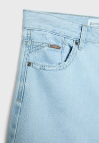 Vaaleansiniset farkut, joissa on repsottavat taskun reunat, metallinen niitti sekä tikkaus yksityiskohdat vyötäröllä ja sivusaumoissa.