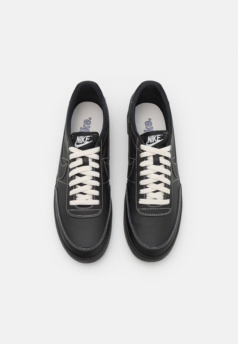 Zapatillas de cuero negro con cordones blancos, puntera redondeada, costuras de contraste y una etiqueta de marca en la lengüeta. Suela de goma y un interior acolchado.