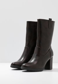 Botas de tobillo de cuero marrón con un acabado texturizado, punta redonda, panel elástico lateral y tacón cuadrado. Diseño minimalista en un color sólido.