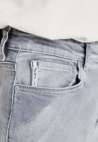 Pilki džinsai turi tradicinį penkių kišenių dizainą su maža etikete gale. Tekstūra atrodo švelni su nedideliu skalbimu.