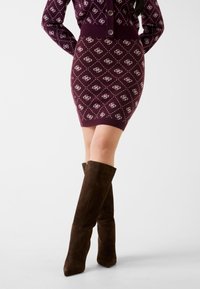 Pletená burgundská tužková sukně s bílým diamantovým vzorem, doplněná hnědými semišovými kozačkami ke kolenům s čtvercovou špičkou a hladkou texturou.