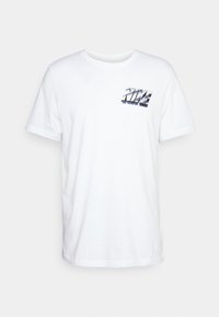 Camiseta de algodón blanca con mangas cortas. Presenta un logo plateado reflectante de "NIKE" en el lado izquierdo del pecho. Diseño clásico de cuello redondo.
