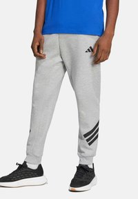 Gray sweatpants with black striped accents, tapered fit, ribbed cuffs, worn with black athletic shoes, and blue T-shirt visible above.