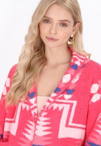 Fleece-Cardigan in leuchtendem Pink mit grafischen Mustern in Weiß und Blau. Bemerkenswerte Merkmale sind der Schalkragen und der strukturierte Stoff.
