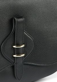 Schwarze Lederhandtasche mit strukturierter Oberfläche, geschwungenen Akzenten und goldfarbenen Beschlägen mit doppelt-ringförmigem Detail am Verschluss.