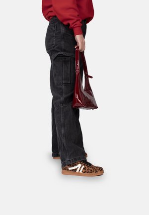 Red patent leather handbag with short handles, paired with black cargo pants and leopard print sneakers with white accents.