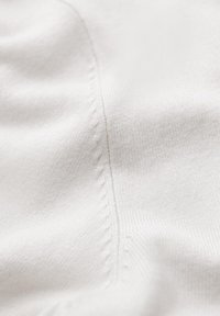 Biała tkanina o miękkiej strukturze i gładkiej powierzchni, z wyraźnym szwem podkreślonym kontrastowym wzorem szycia.