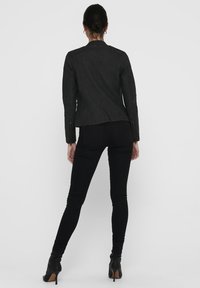 Veste en cuir noir avec un détail matelassé sur les manches, design ajusté et coupe droite, associée à un jean skinny noir et des bottes à talons.
