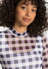 Tshirt de mangas longas com padrão xadrez em roxo, castanho e branco, feito de um material leve e semi-transparente. Decote alto.