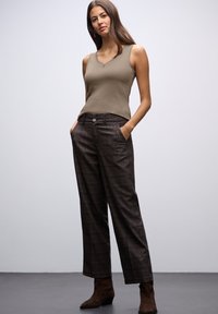 Top in verde oliva con scollo a V, abbinato a pantaloni larghi a quadri marroni e stivaletti alla caviglia marroni. Tessuto morbido, vestibilità comoda.