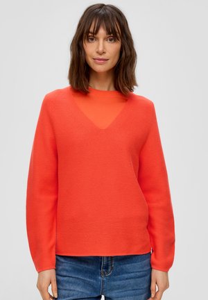 Sweter z dekoltem w serek, z długim rękawem, w jasnym pomarańczowym kolorze z dzianiny. Luźny krój, fakturowana powierzchnia, zestawiony z niebieskimi dżinsami.