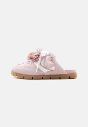 Pink slip-on sneaker with white laces, heart-shaped charm, tassel detail, white stripe accents, and brown grooved sole.