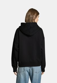 Felpa nera con cappuccio, dal fitting rilassato, tessuto morbido e polsini a costine. Presenta una tasca a marsupio e un design liscio e senza decorazioni.