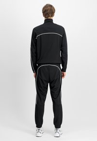 Juodas sportinis treningas su baltais apvadais. Yra užtrauktuko apykaklė ir siaurėjantys kelnes. Derinamas su baltais ir pilkais sportiniais batais.