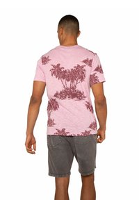 T-shirt rosa a maniche corte realizzata in tessuto testurizzato, con un motivo di palme rosso scuro sul retro. Abbinata a pantaloni corti grigi.