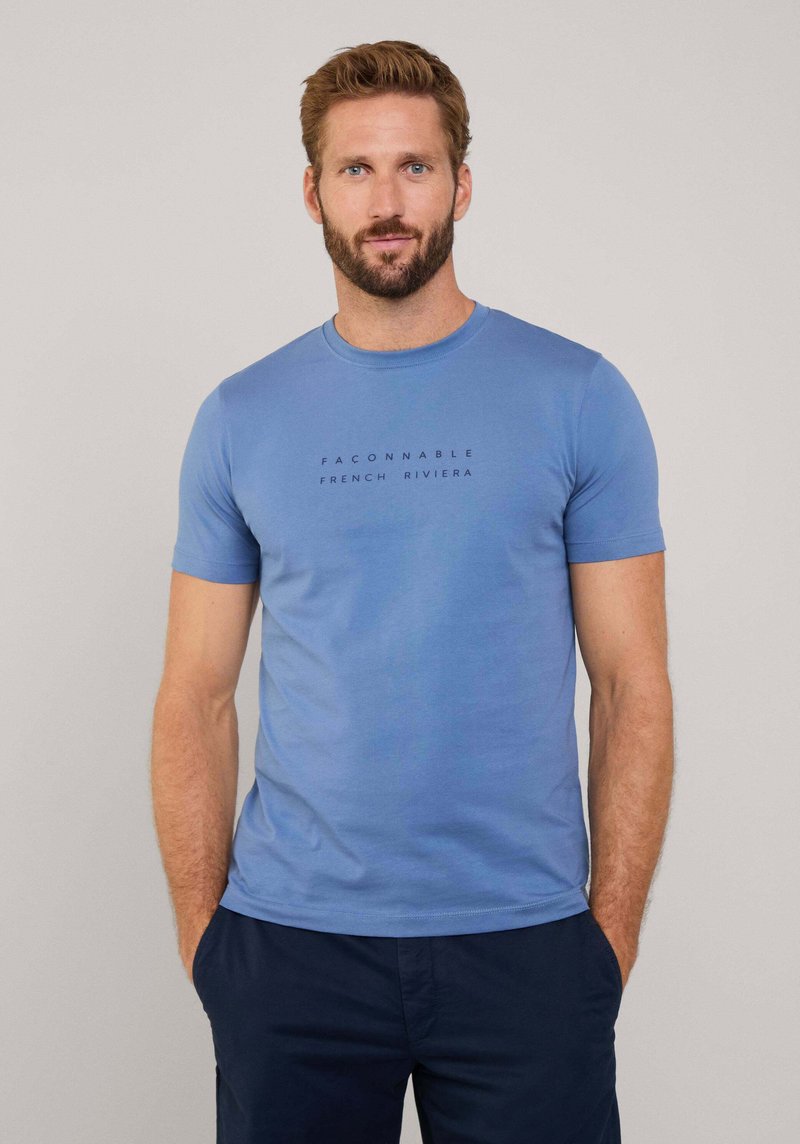 Camiseta de algodón azul con cuello redondo, mangas cortas y el texto "FACONNABLE FRENCH RIVIERA" impreso en negro en la parte delantera.