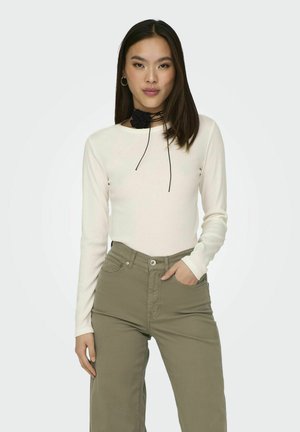 Crème lange mouwen top met een aansluitend ontwerp, gecombineerd met olijfgroene hoge taillebroek. Zwarte choker details accentueren de halslijn.