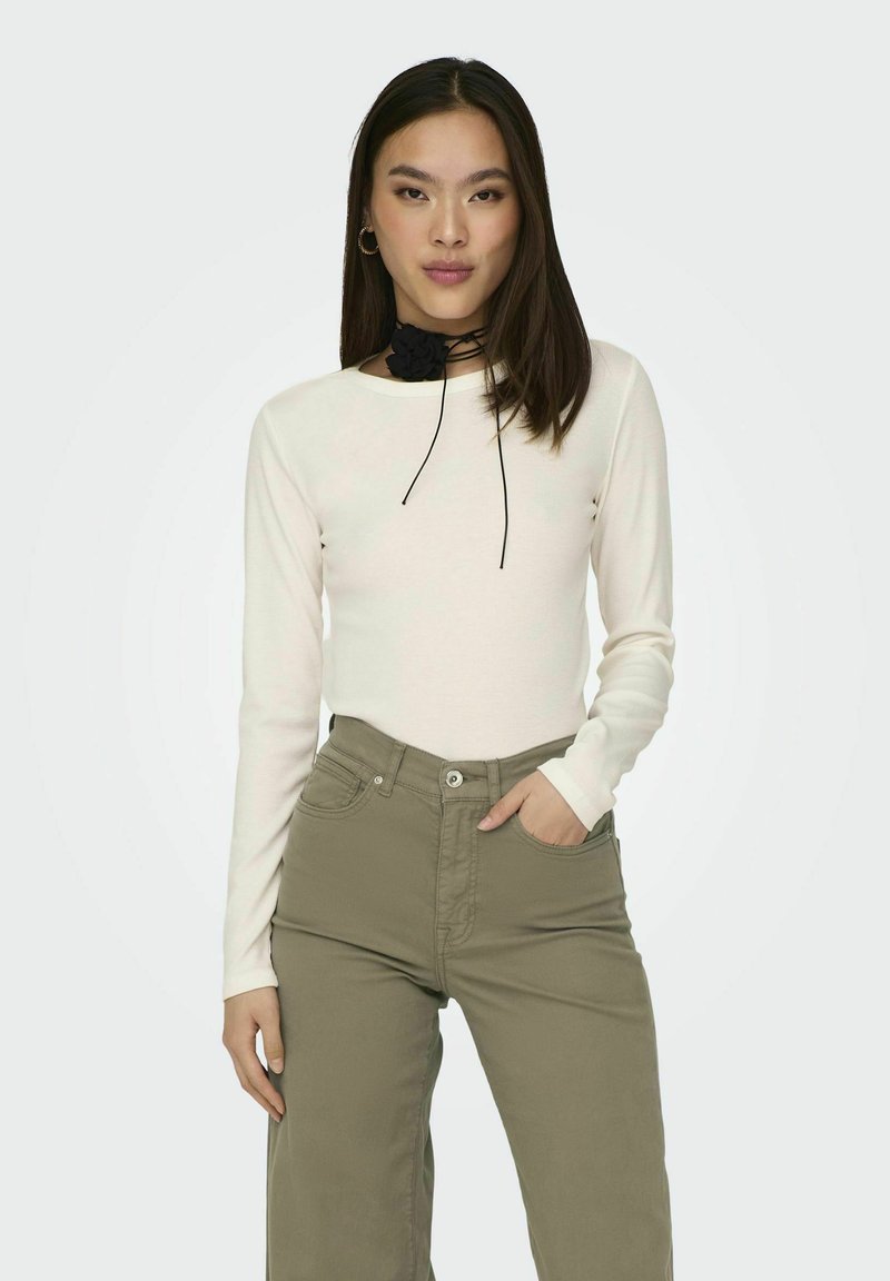 Crème lange mouwen top met een aansluitend ontwerp, gecombineerd met olijfgroene hoge taillebroek. Zwarte choker details accentueren de halslijn.