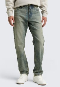 Jeans de mezclilla azul claro con un corte recto, lavado desgastado y sutiles arrugas. Combinados con zapatillas blancas para un contraste.
