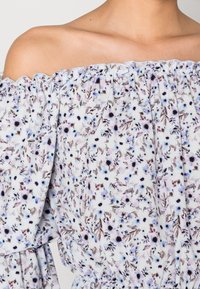 Květinová off-the-shoulder blůza ve světle modré látce, s fialovými a černými květinovými vzory, elastickým výstřihem a nabíranými rukávy.