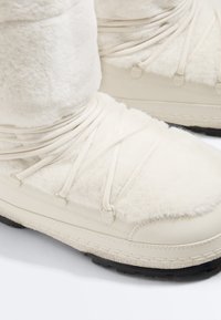 Bottes d'hiver blanches avec tissu doux et duveteux, lacets croisés et semelles épaisses en caoutchouc noir pour une bonne traction.