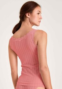 Roze geribbelde tanktop met gekantte kantafwerking op de schouderbandjes, een getailleerd ontwerp en een soepele textuur. Getoond vanuit een zijaanzicht.