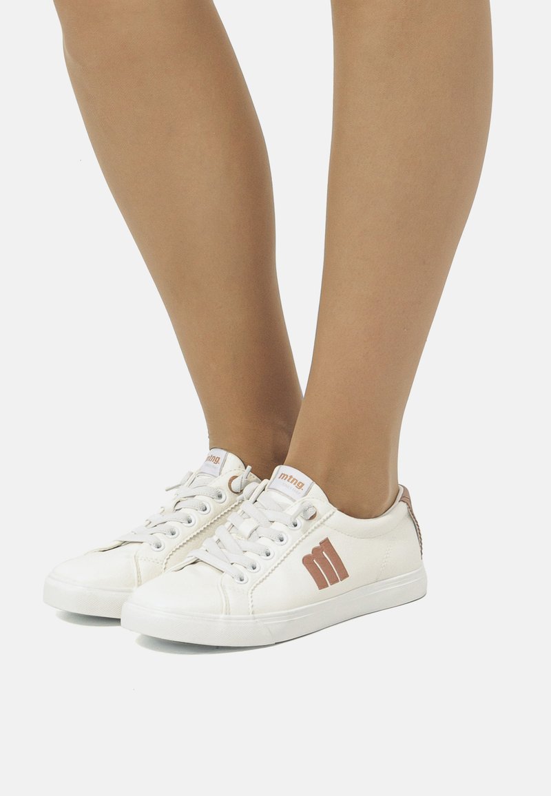 Baskets en toile blanches avec des orteils ronds, présentant des accents brun clair, un design à lacets et un détail de logo sur les côtés extérieurs.