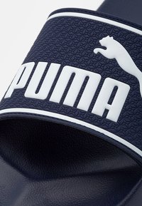 Sandale à glissière bleu marine avec une sangle texturée arborant le logo "PUMA" en blanc et la silhouette du chat, semelle en caoutchouc lisse, design minimaliste.