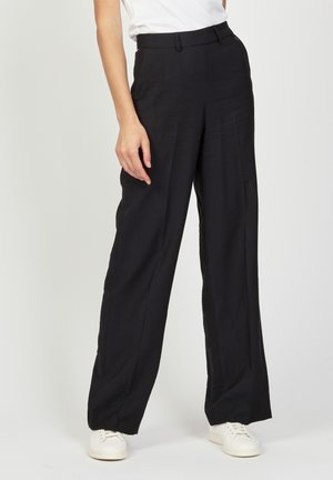 Black, high-waisted, wide-leg pants in a smooth fabric with a tailored design. Paired with white sneakers for a casual look.