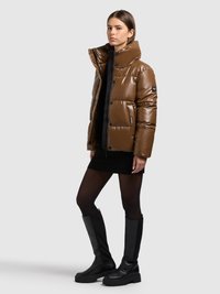 Brun vadderad jacka med hög krage, glansigt yttre och stora knappar. Kombinerad med en svart ribbad klänning och knähöga svarta stövlar.