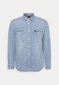 Světle modrá džínová košile s dlouhými rukávy, zapínáním na knoflíky vpředu, dvěma náprsními kapsami a špičatým límcem. Obsahuje stehací detaily a značkovou etiketu.