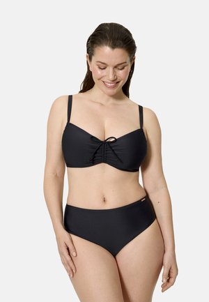 Mujer sonriente con el cabello mojado que lleva un bañador de dos piezas negro con tirantes ajustables y un detalle fruncido en forma de lazo en la parte superior.