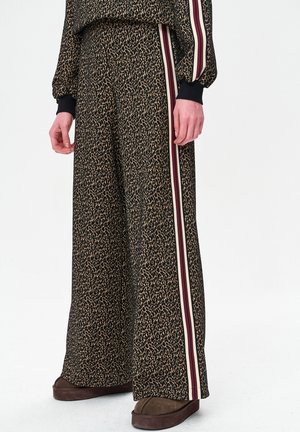 Spodnie z szerokimi nogawkami w czarno-brązowy nadruk w panterkę z kontrastującymi pionowymi paskami w kolorach czerwonym, kremowym i granatowym po bokach. Miękka tekstura.