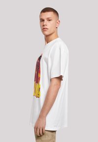 Bílý bavlněný tričko s barevným grafickým potiskem a oversized střihem. Krátké rukávy, kulatý výstřih, žádné viditelné loga ani ozdoby.