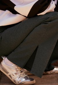 Pantalones grises con aberturas laterales, combinados con zapatillas plateadas brillantes y calcetines blancos hasta el tobillo. La tela parece suave con una textura lisa.