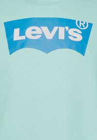 Blå Levi's-logga med vit text på ljus turkos tygbakgrund.