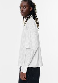 Witte gestreepte oversized shirt met een relaxte pasvorm, lange mouwen en knoopmanchetten, gedragen met donkere spijkerbroeken.