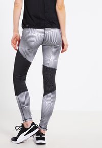 Sorte og hvide leggings med geometriske mønstre, teksturerede mesh-paneler og tætsiddende design. Båret med sorte træningssko.