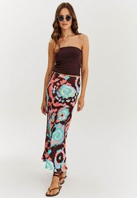 Hnedý vrch bez ramienok v kombinácii s dlhou, vzorovanou sukňou s vírmi v ružovej, tyrkysovej a čiernej farbe. Modelka má na sebe hnedé sandále a slnečné okuliare.